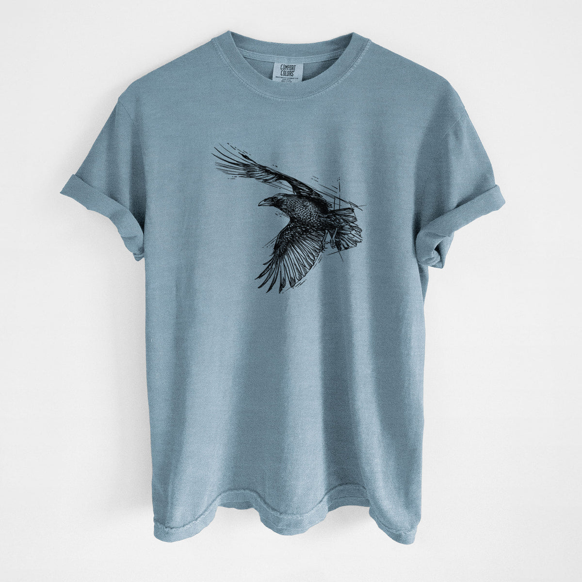 Steel blue Comfort Colors t-shirt laid flat, printed with a black ink illustration of a raven in flight with its wings spread.