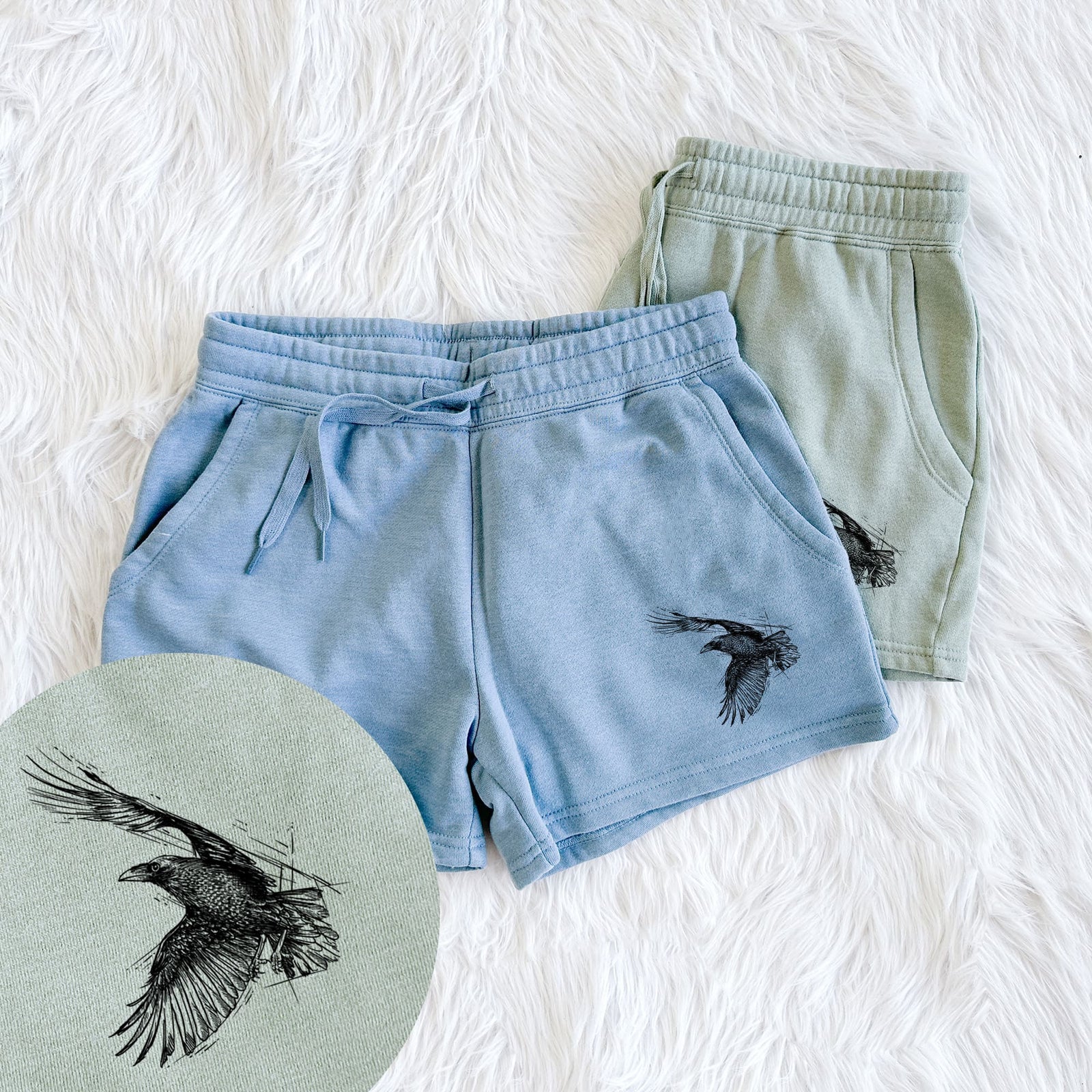 Two pairs of Cali Wave shorts in different colors printed with a black ink illustration of a raven in flight with its wings spread, with a close-up of the print.