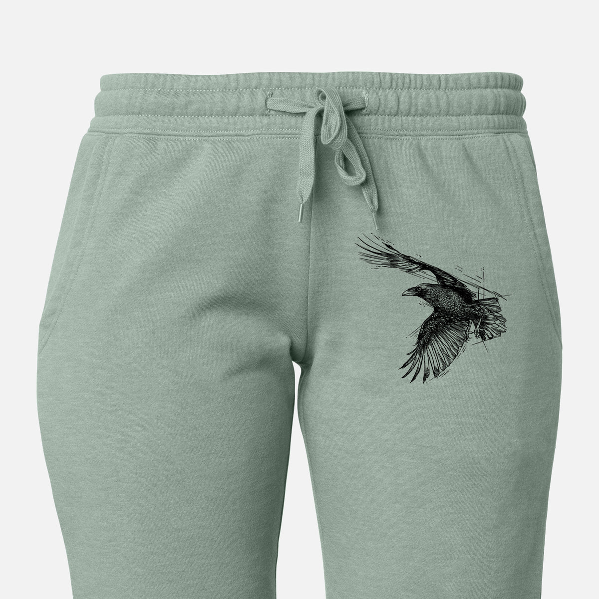 Front of sage green Cali Wave sweatpants, printed with a black ink illustration of a raven in flight with its wings spread on the leg.