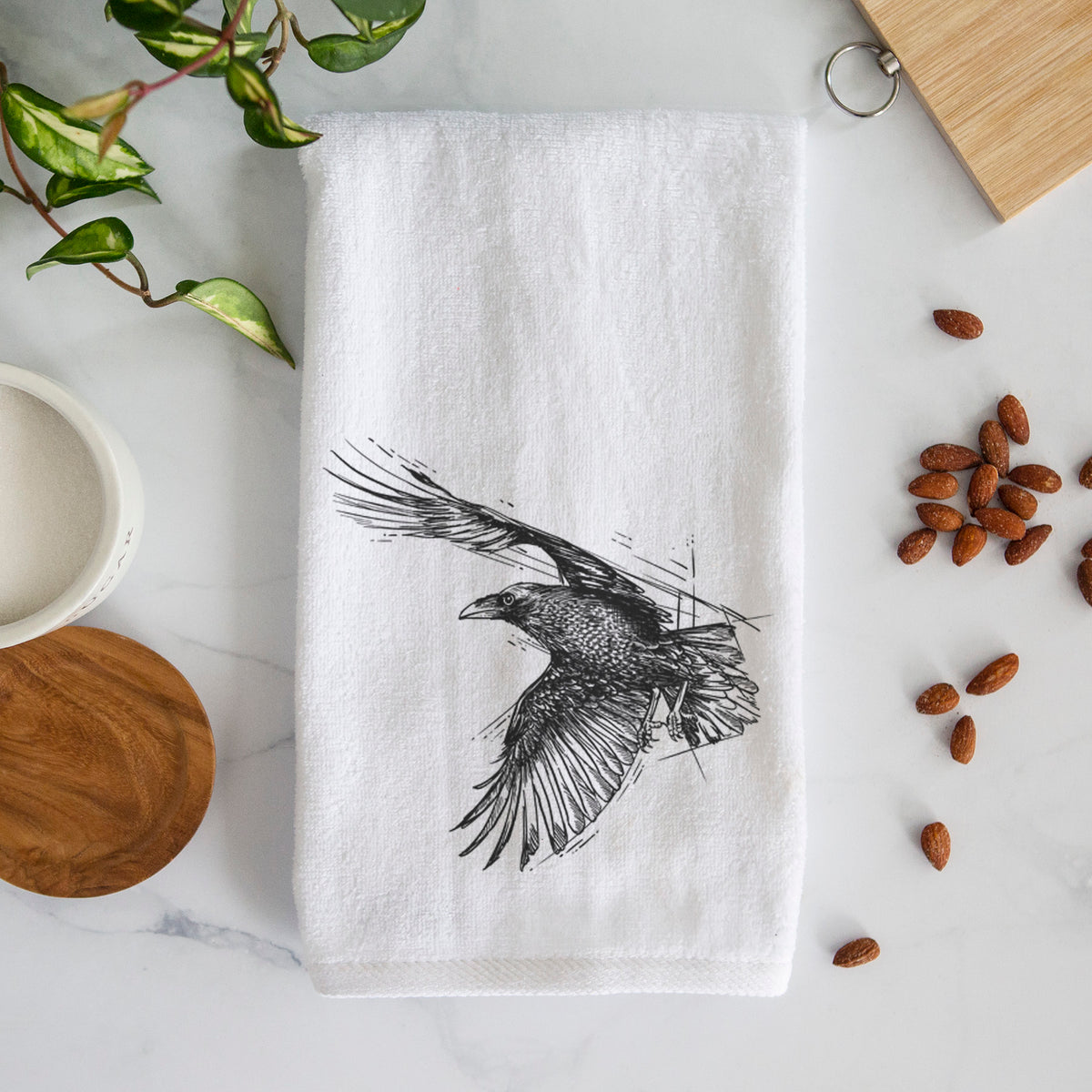 White hand towel printed with a black ink illustration of a raven in flight with its wings spread.