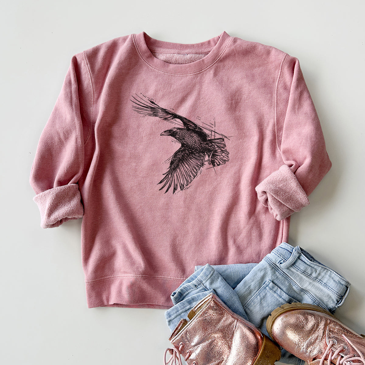 Youth crewneck sweatshirt printed with a black ink illustration of a raven in flight with its wings spread, styled flat with jeans and boots.