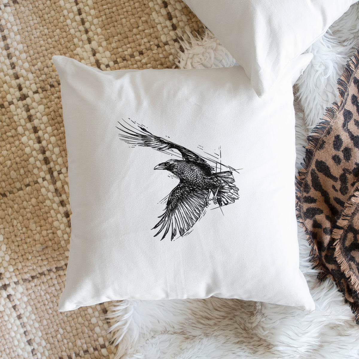 White pillow cover printed with a black ink illustration of a raven in flight with its wings spread, on a woven chair.