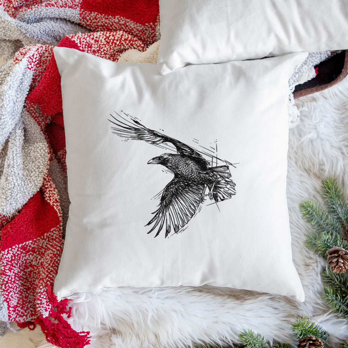 White pillow cover printed with a black ink illustration of a raven in flight with its wings spread, on a woven chair.