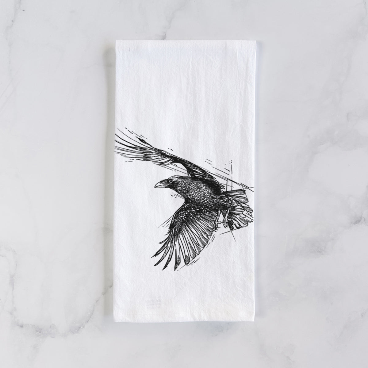 White cotton tea towel laid flat on marble, printed with a black ink illustration of a raven in flight with its wings spread.