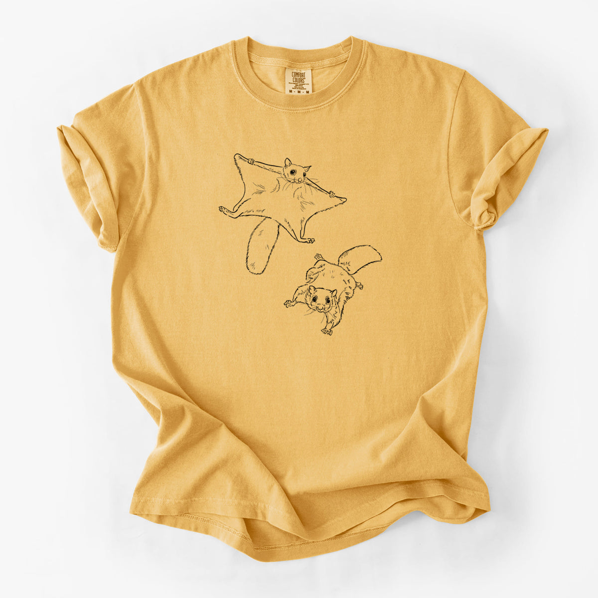 Golden wheat yellow Comfort Colors t-shirt laid flat, printed with a black ink illustration of two flying squirrels gliding with their skin flaps spread.