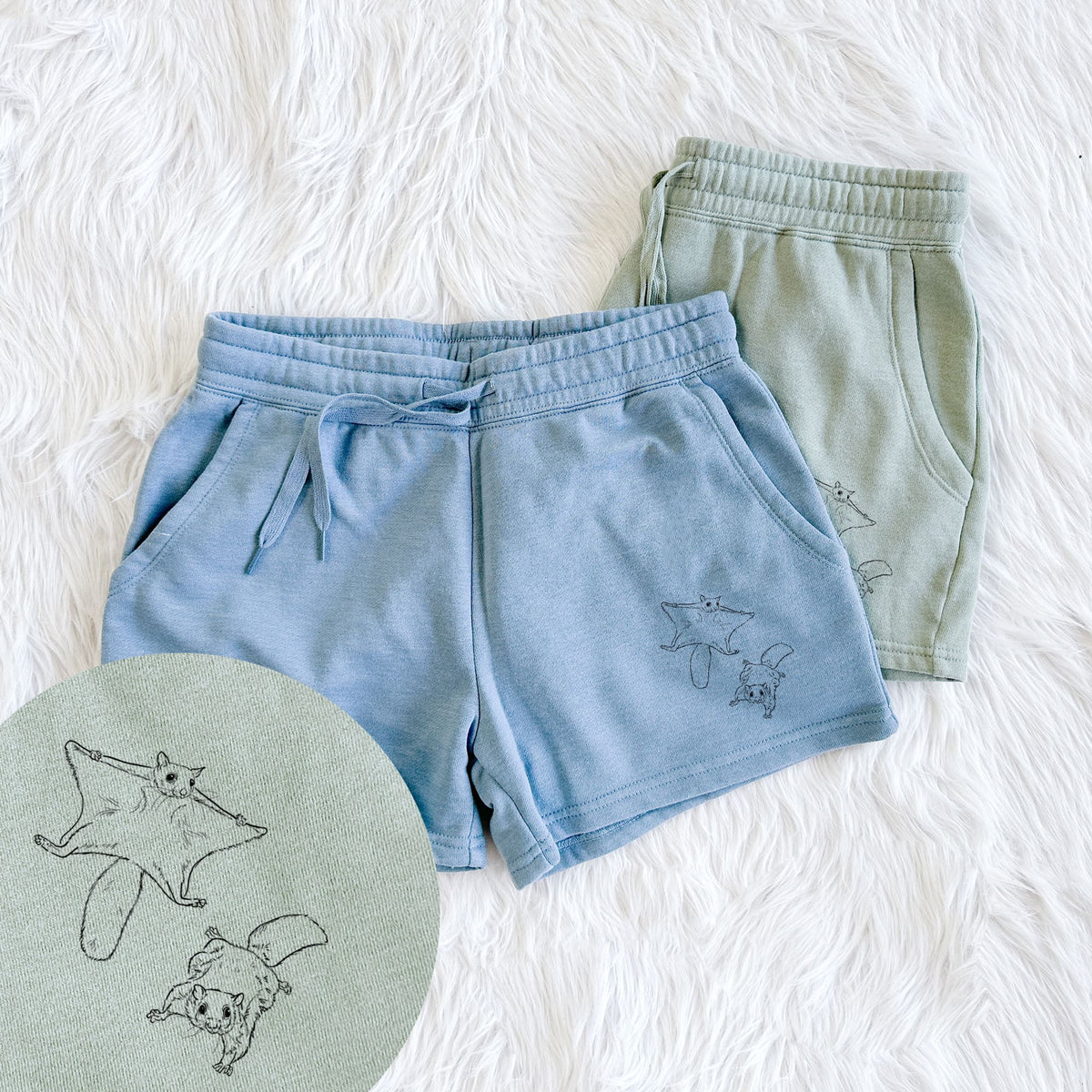 Two pairs of Cali Wave shorts in different colors printed with a black ink illustration of two flying squirrels gliding with their skin flaps spread, with a close-up of the print.