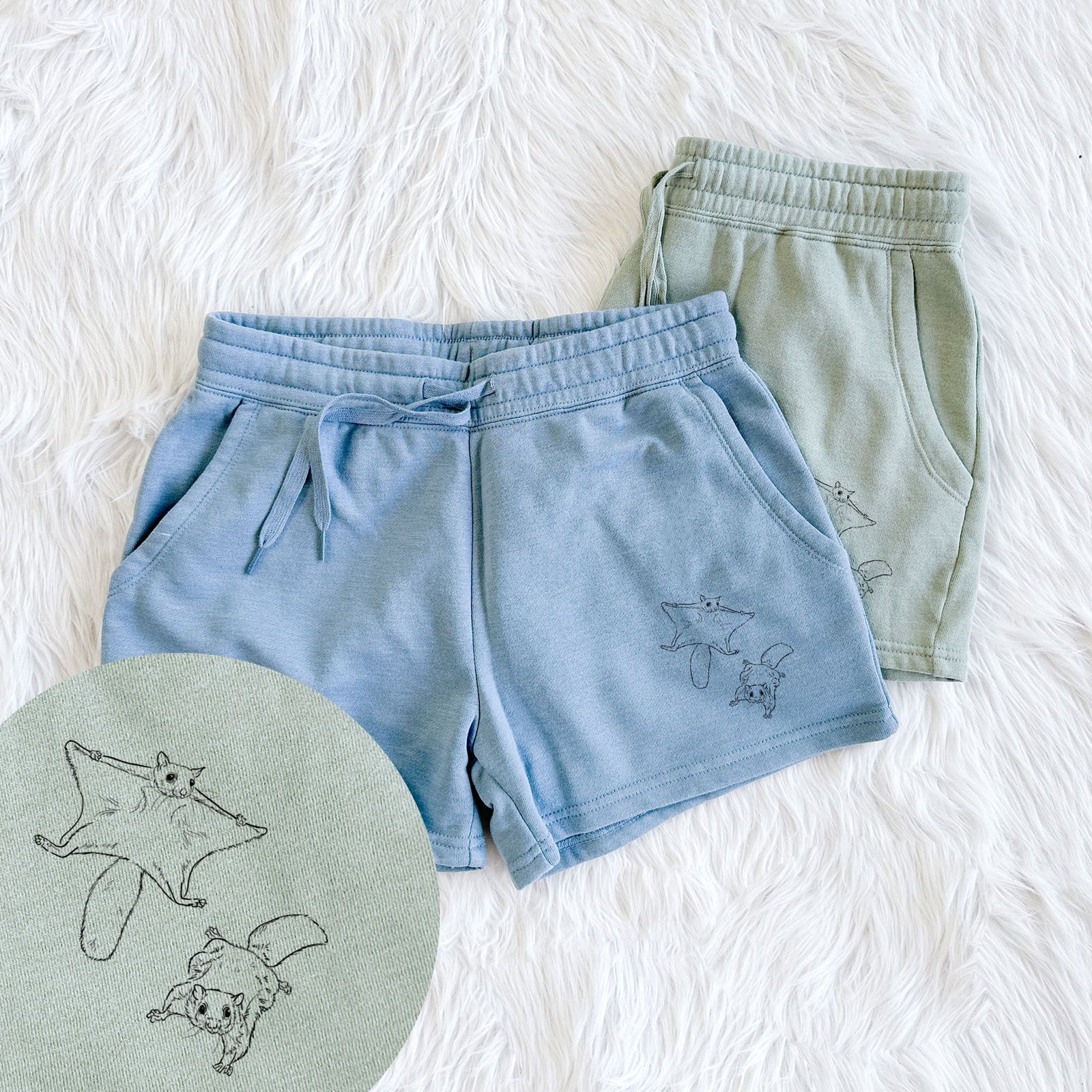 Two pairs of Cali Wave shorts in different colors printed with a black ink illustration of two flying squirrels gliding with their skin flaps spread, with a close-up of the print.