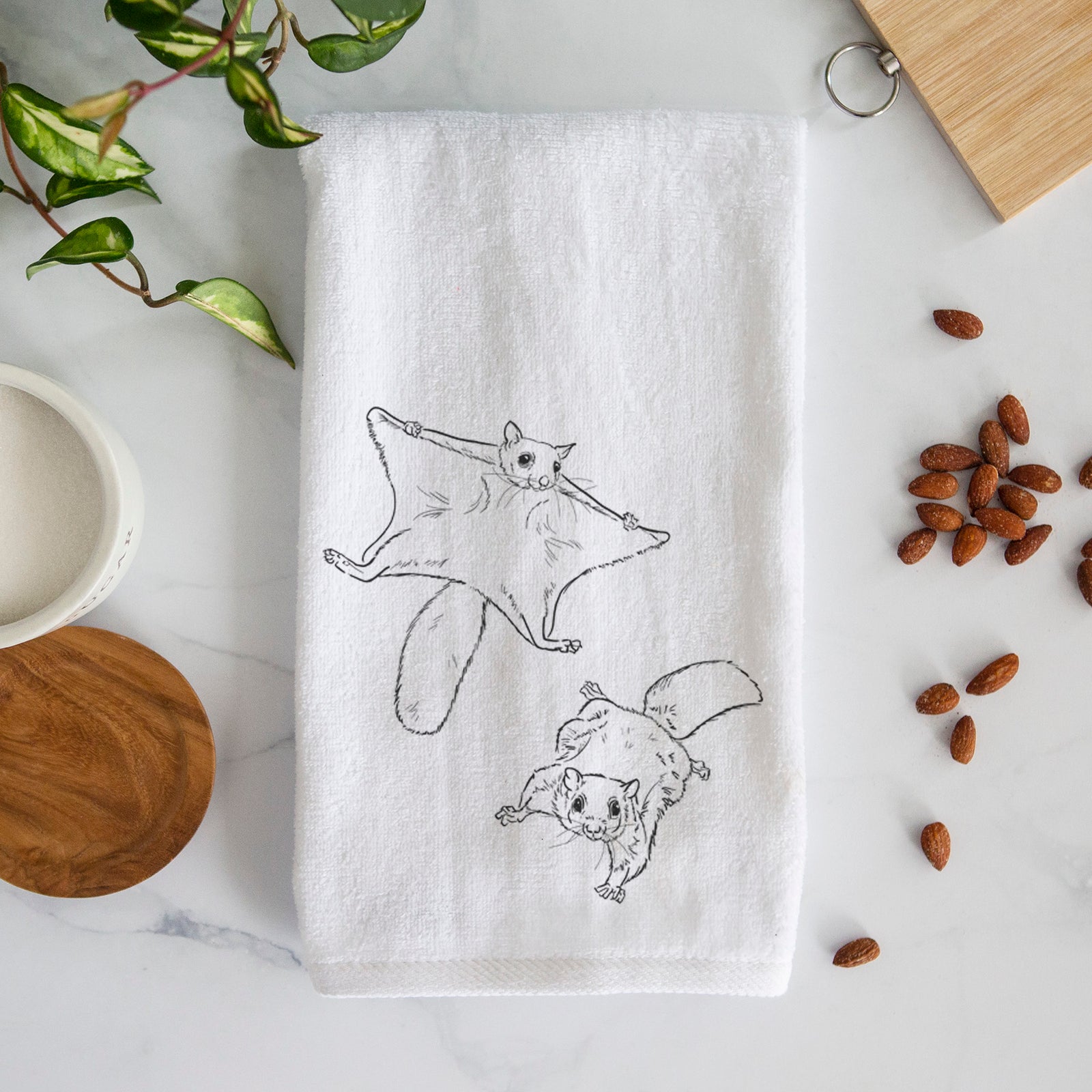 White hand towel printed with a black ink illustration of two flying squirrels gliding with their skin flaps spread.
