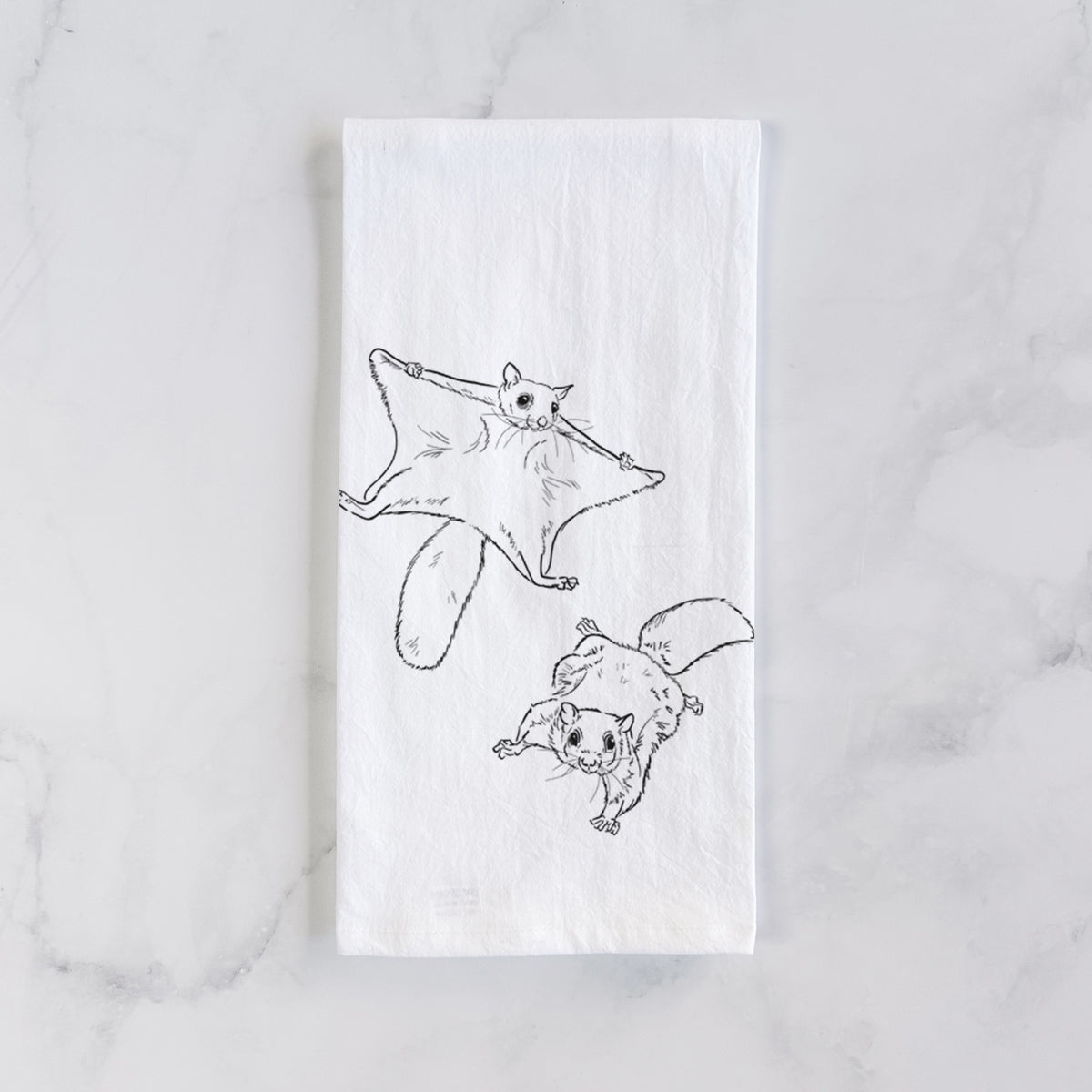White cotton tea towel laid flat on marble, printed with a black ink illustration of two flying squirrels gliding with their skin flaps spread.