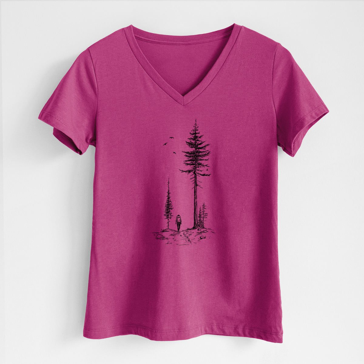 Berry pink women's relaxed fit cotton V-neck t-shirt laid flat, printed with a black ink illustration of a lone hiker walking between tall pine trees with birds overhead.
