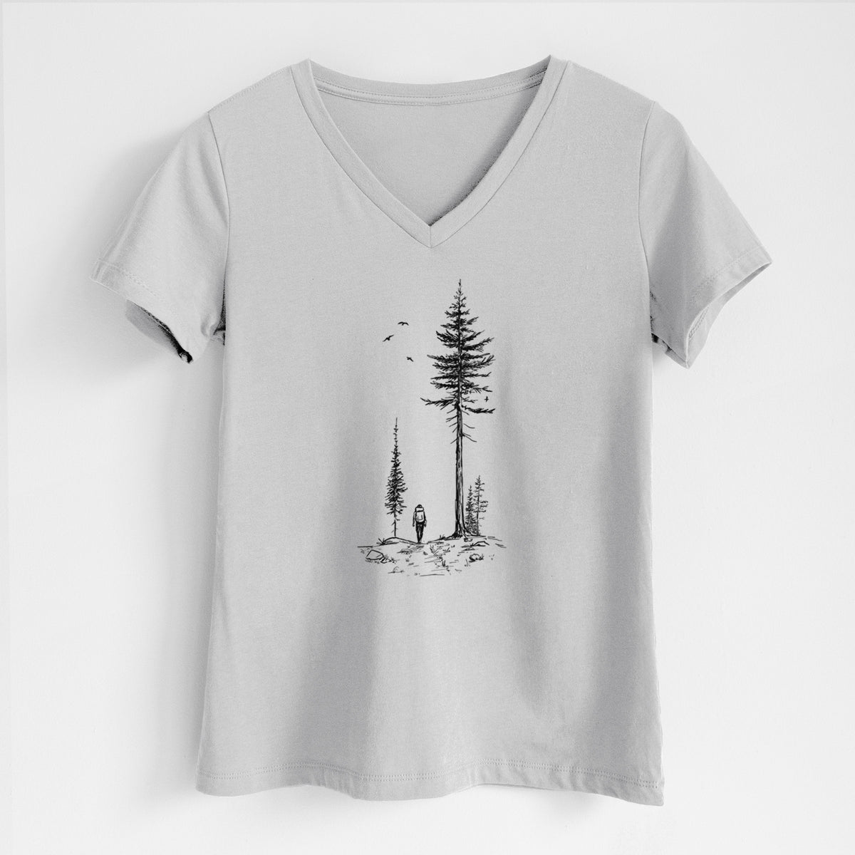 Lunar grey women's relaxed fit cotton V-neck t-shirt laid flat, printed with a black ink illustration of a lone hiker walking between tall pine trees with birds overhead.