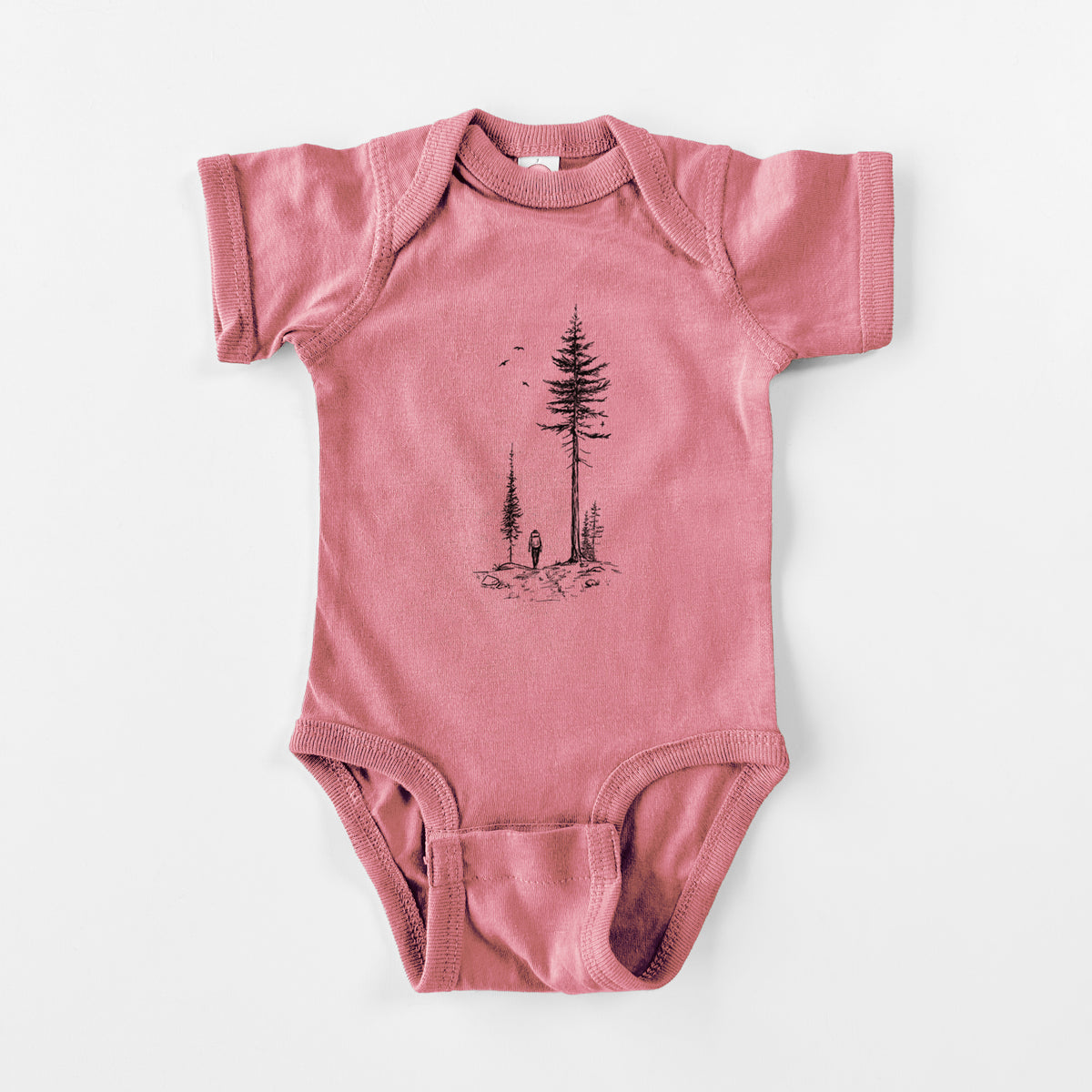 Mauve pink baby bodysuit laid flat, printed with a black ink illustration of a lone hiker walking between tall pine trees with birds overhead.