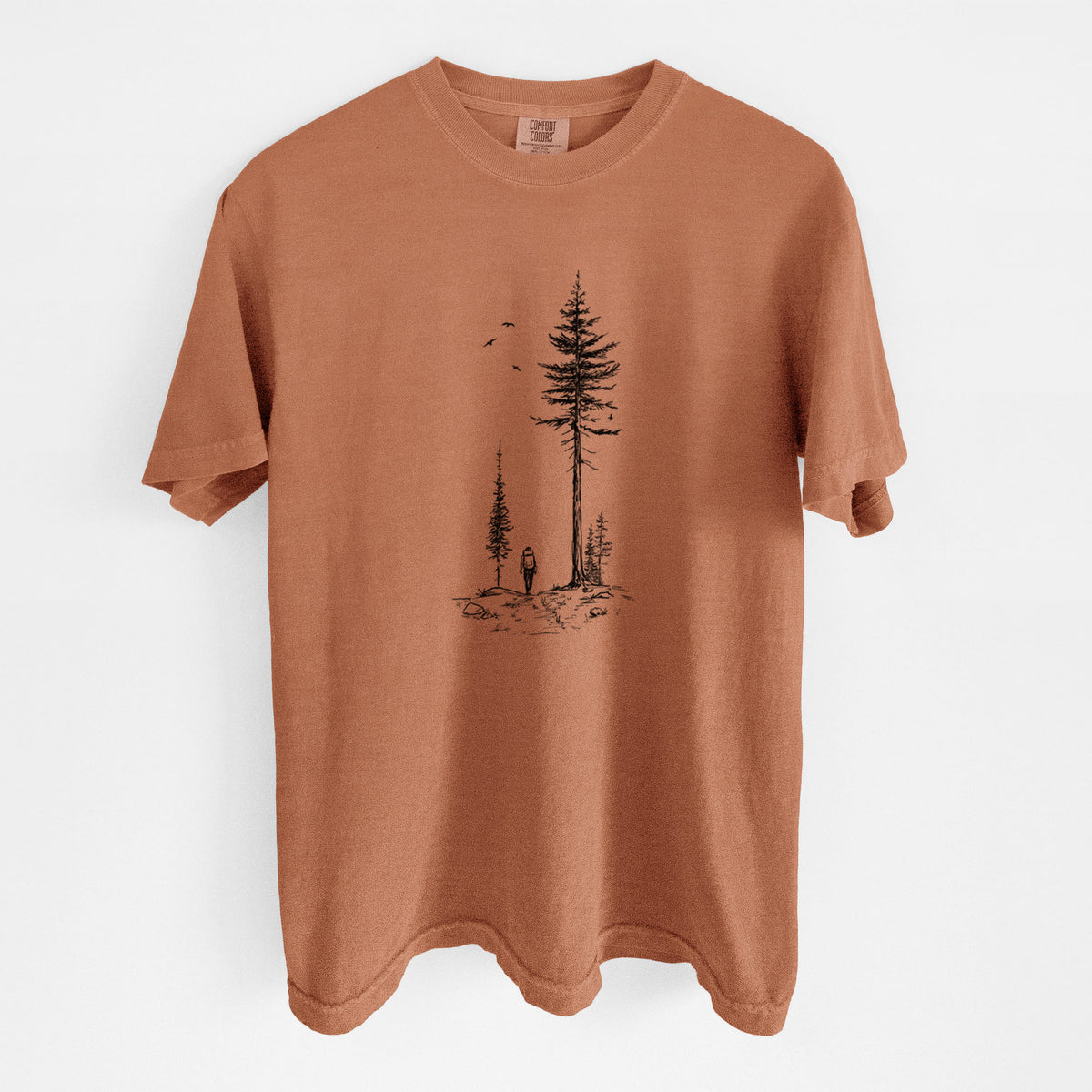 Yam burnt orange Comfort Colors t-shirt laid flat, printed with a black ink illustration of a lone hiker walking between tall pine trees with birds overhead.