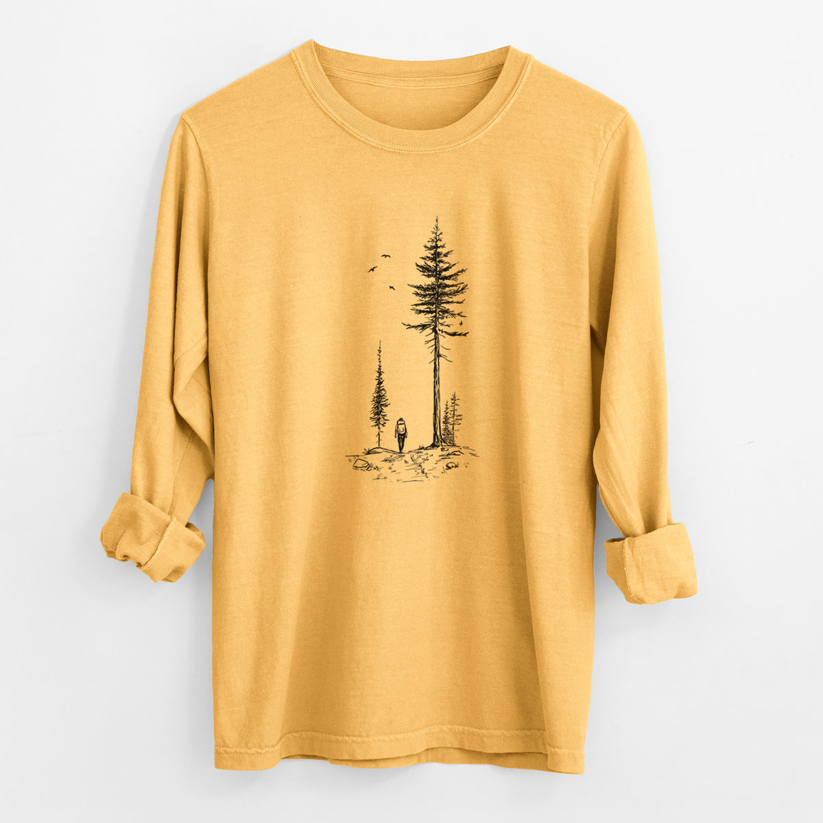 Golden wheat yellow Comfort Colors long sleeve shirt laid flat with the cuffs rolled, printed with a black ink illustration of a lone hiker walking between tall pine trees with birds overhead.