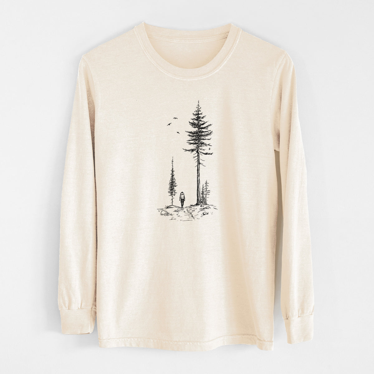 Ivory Comfort Colors long sleeve shirt laid flat, printed with a black ink illustration of a lone hiker walking between tall pine trees with birds overhead.