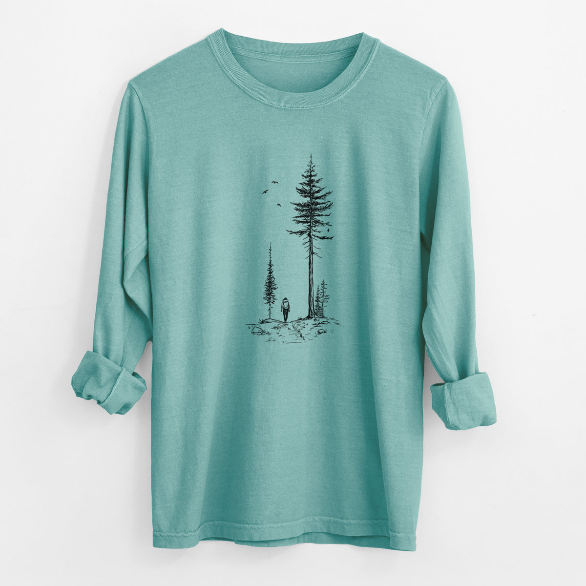 Reef green Comfort Colors long sleeve shirt laid flat with the cuffs rolled, printed with a black ink illustration of a lone hiker walking between tall pine trees with birds overhead.