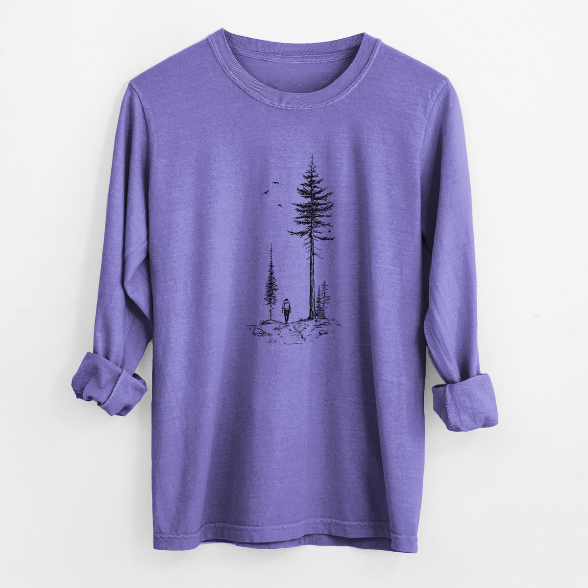 Violet purple Comfort Colors long sleeve shirt laid flat with the cuffs rolled, printed with a black ink illustration of a lone hiker walking between tall pine trees with birds overhead.