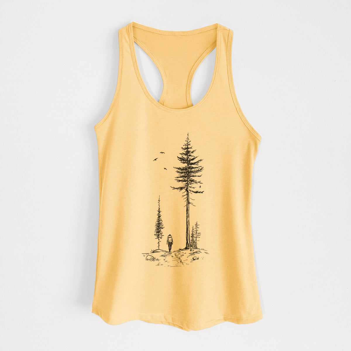Banana cream women's racerback tank top laid flat, printed with a black ink illustration of a lone hiker walking between tall pine trees with birds overhead.