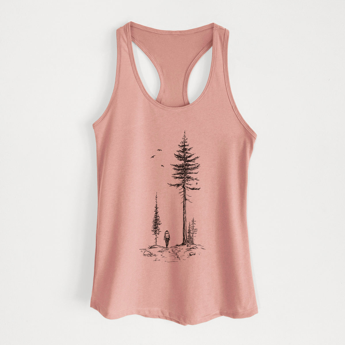 Desert pink women's racerback tank top laid flat, printed with a black ink illustration of a lone hiker walking between tall pine trees with birds overhead.