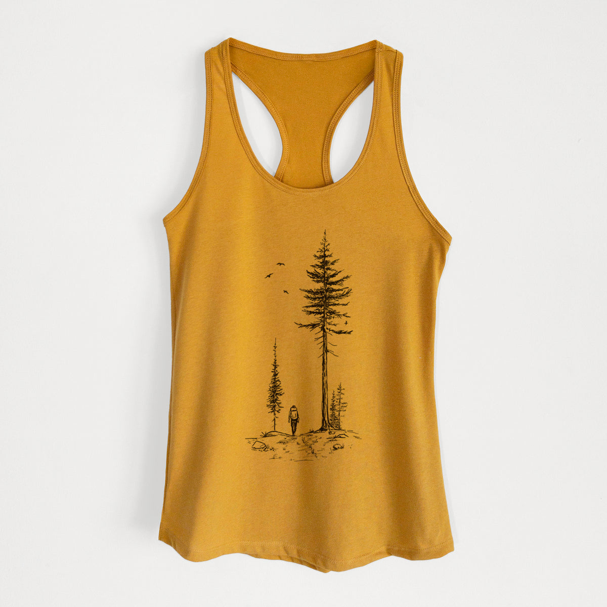 Gold women's racerback tank top laid flat, printed with a black ink illustration of a lone hiker walking between tall pine trees with birds overhead.