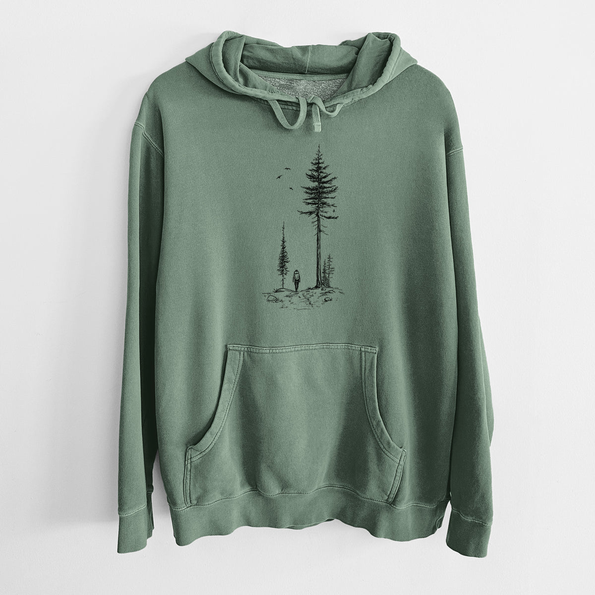 Alpine green pigment dyed hoodie laid flat, printed with a black ink illustration of a lone hiker walking between tall pine trees with birds overhead.