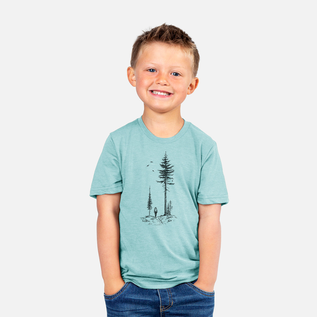 Smiling boy wearing a youth t-shirt printed with a black ink illustration of a lone hiker walking between tall pine trees with birds overhead.