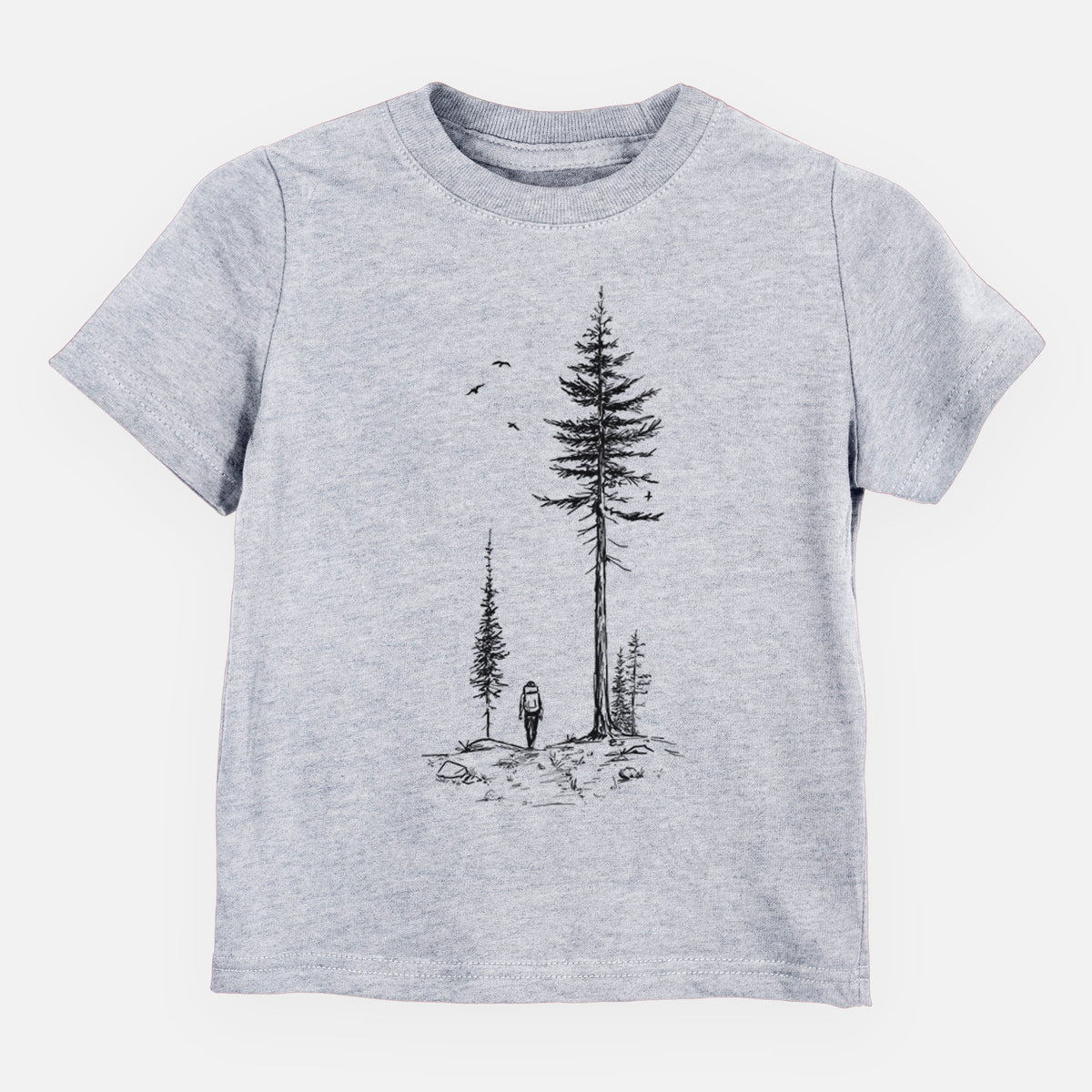 Heather grey toddler t-shirt laid flat, printed with a black ink illustration of a lone hiker walking between tall pine trees with birds overhead.
