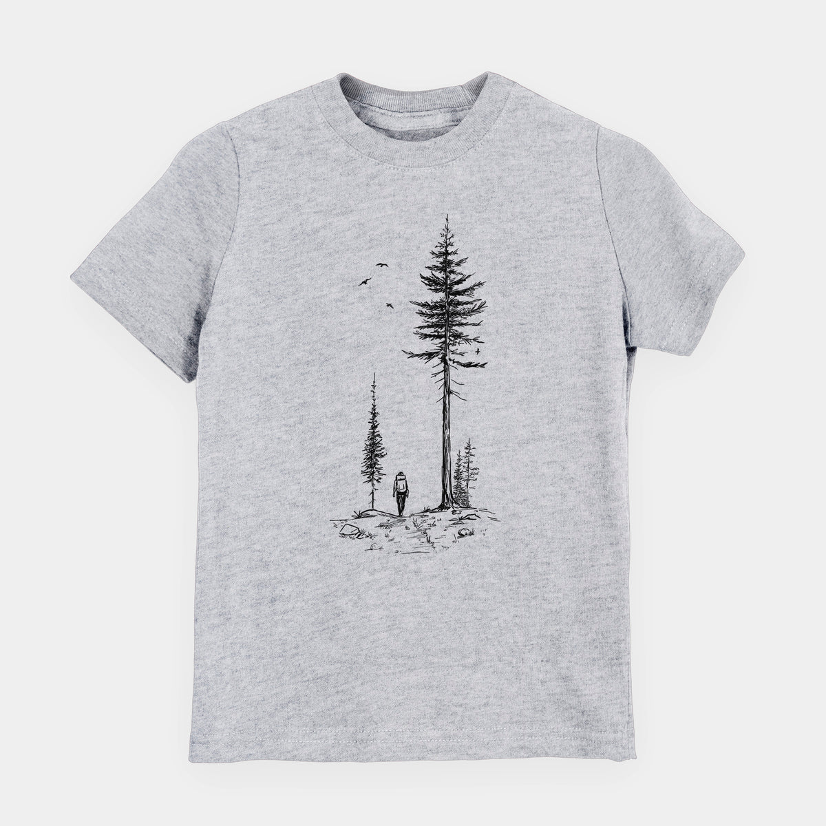 Heather grey youth t-shirt laid flat, printed with a black ink illustration of a lone hiker walking between tall pine trees with birds overhead.