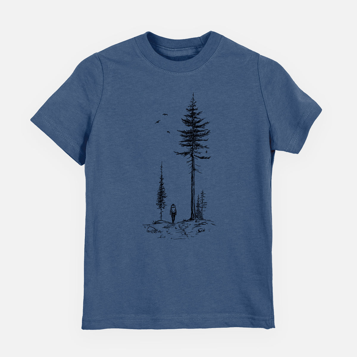 Indigo blue youth t-shirt laid flat, printed with a black ink illustration of a lone hiker walking between tall pine trees with birds overhead.