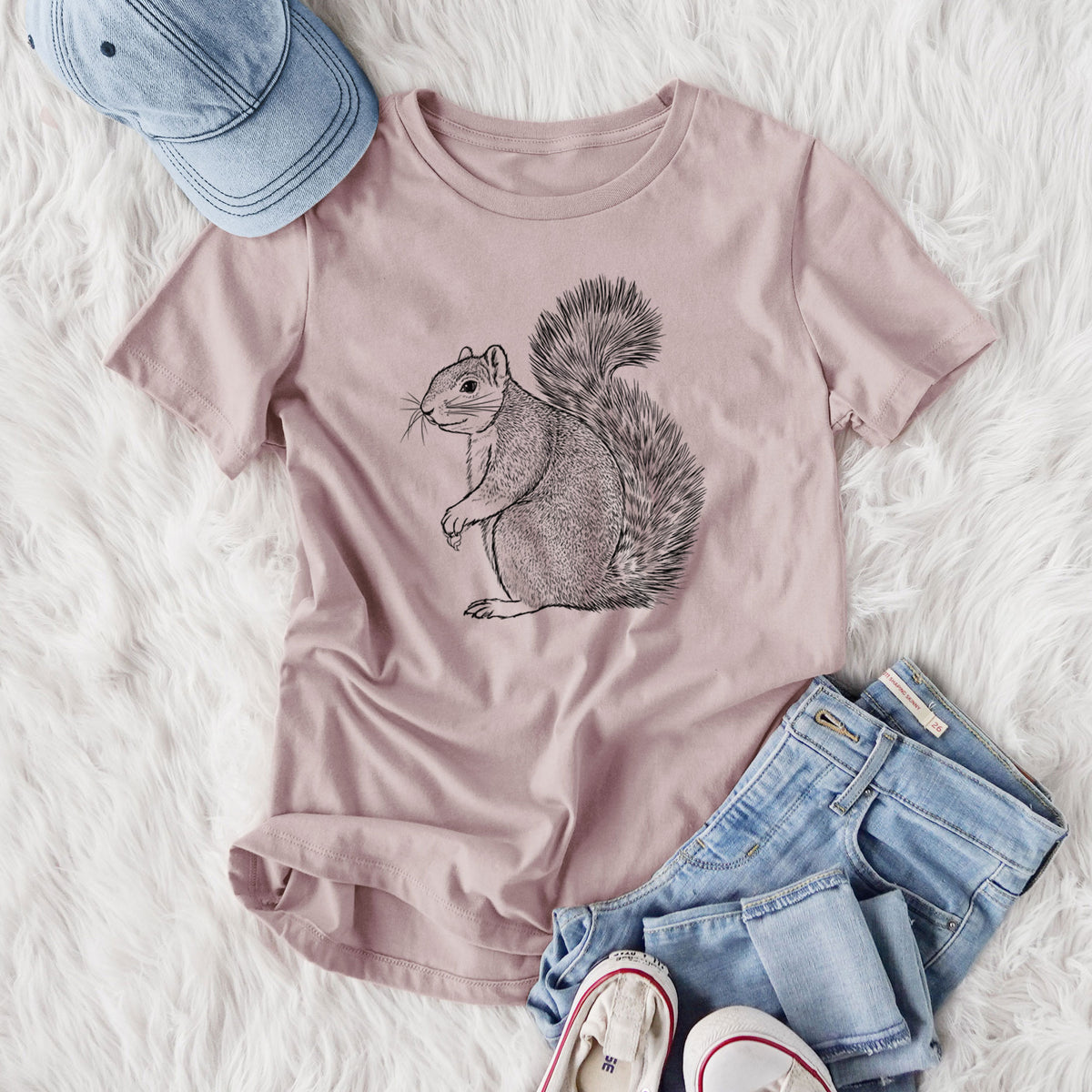 Women's relaxed fit cotton t-shirt printed with a detailed black ink illustration of a fox squirrel sitting with a bushy tail, styled flat on a white faux fur rug with jeans.