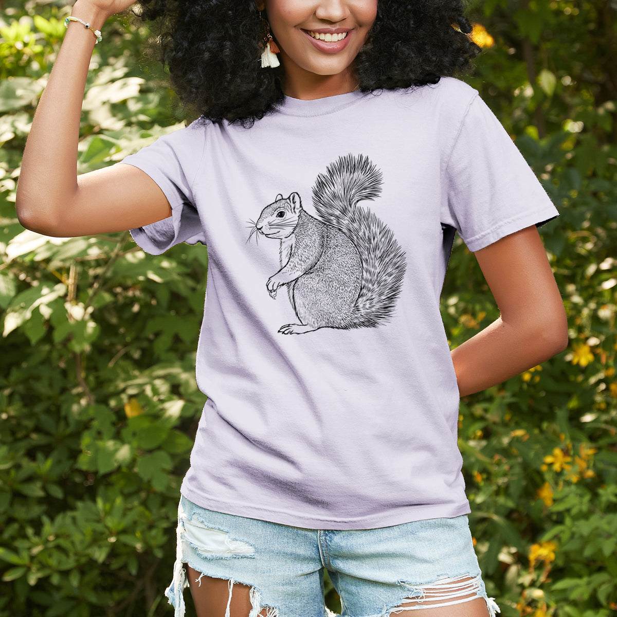 Woman wearing a Comfort Colors t-shirt printed with a detailed black ink illustration of a fox squirrel sitting with a bushy tail, outdoors.