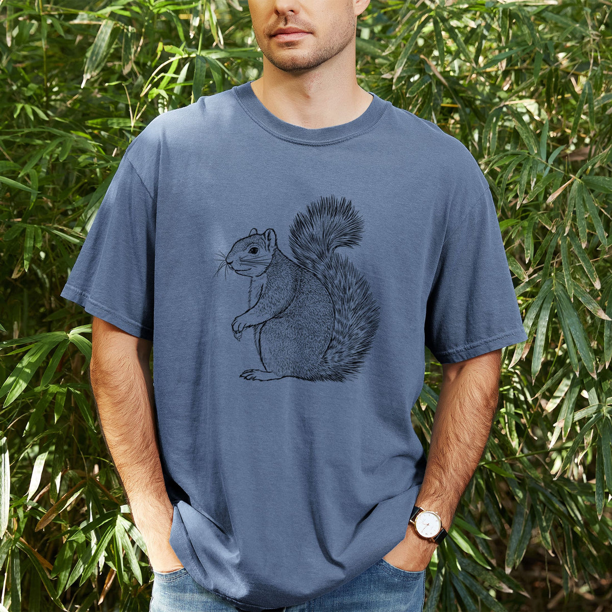 Man wearing a Comfort Colors t-shirt printed with a detailed black ink illustration of a fox squirrel sitting with a bushy tail, outdoors.