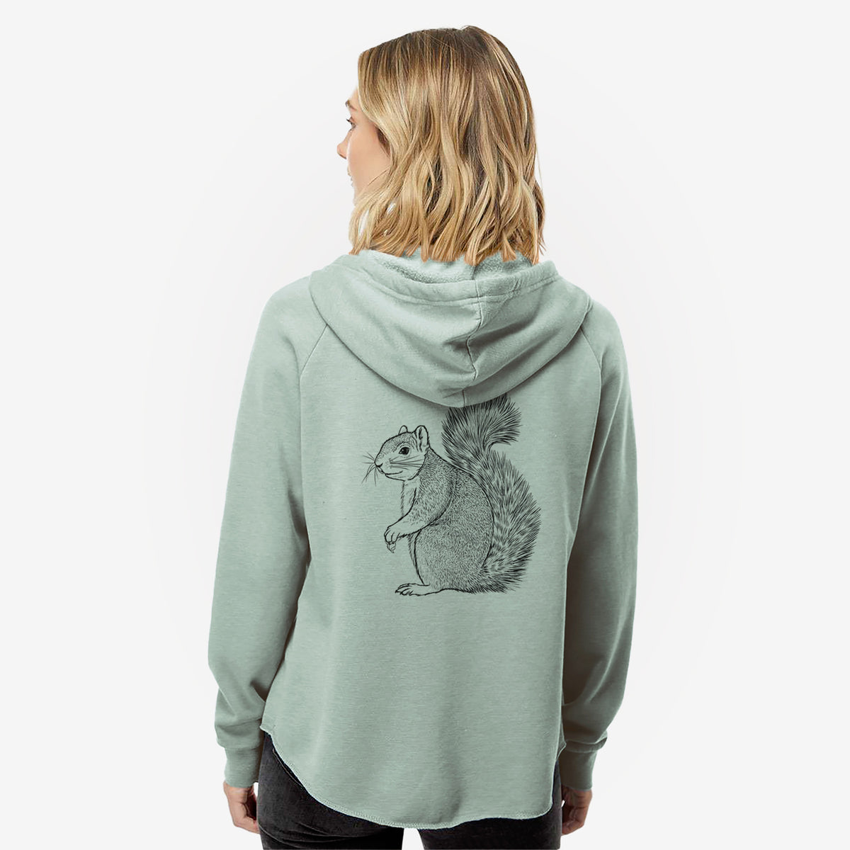 Woman wearing a sage green women's Cali Wave zip-up sweatshirt printed with a detailed black ink illustration of a fox squirrel sitting with a bushy tail, seen from behind.