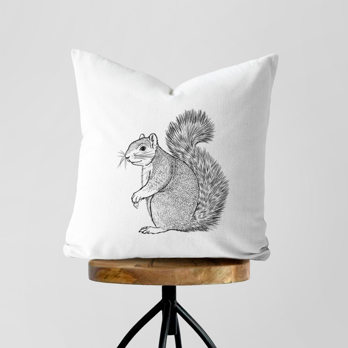 White pillow cover printed with a detailed black ink illustration of a fox squirrel sitting with a bushy tail, on a wooden stool.