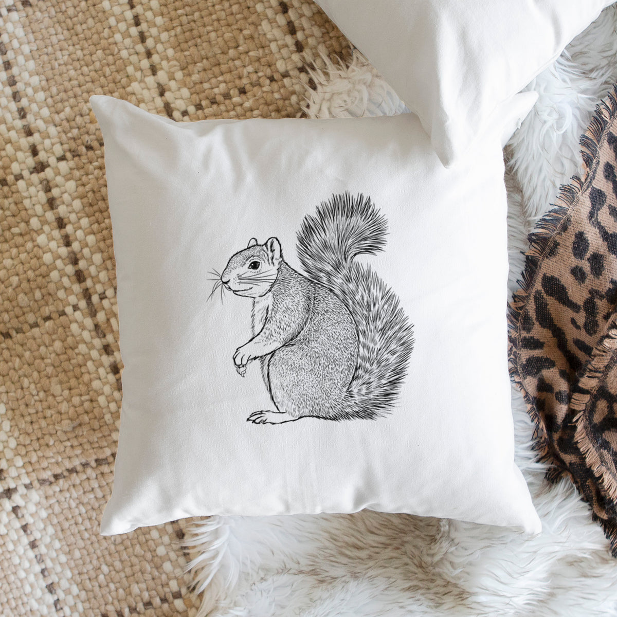 White pillow cover printed with a detailed black ink illustration of a fox squirrel sitting with a bushy tail, on a woven chair.