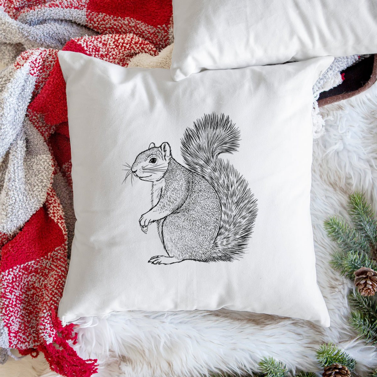 White pillow cover printed with a detailed black ink illustration of a fox squirrel sitting with a bushy tail, on a woven chair.