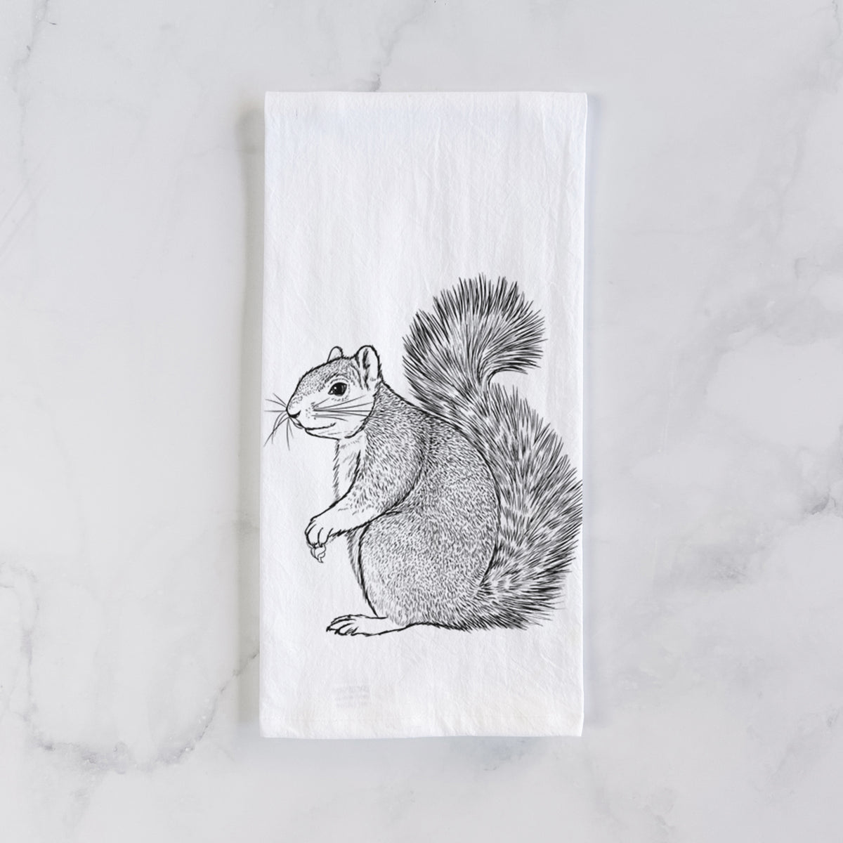 White cotton tea towel laid flat on marble, printed with a detailed black ink illustration of a fox squirrel sitting with a bushy tail.