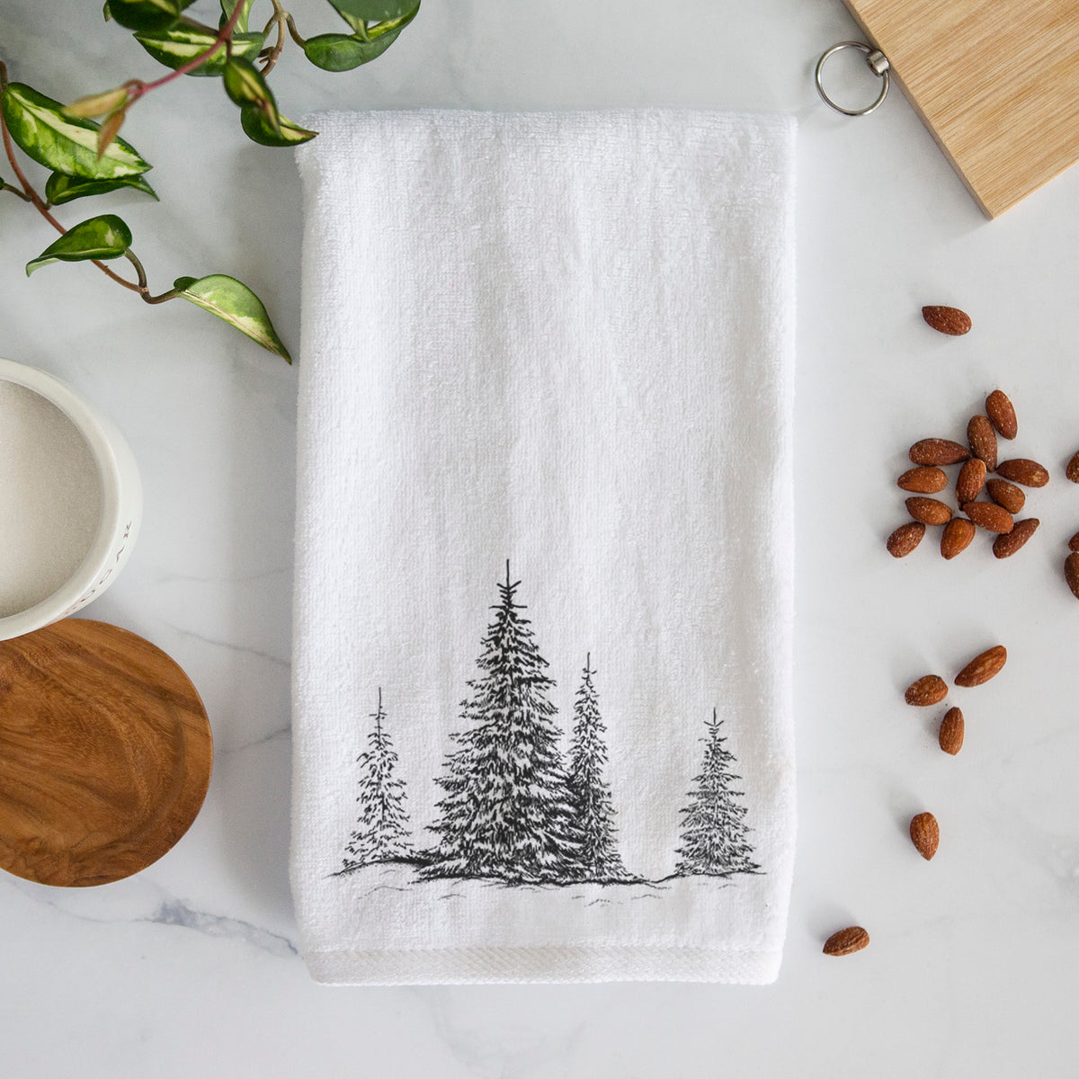 White hand towel printed with a black ink illustration of frost-covered evergreen trees.