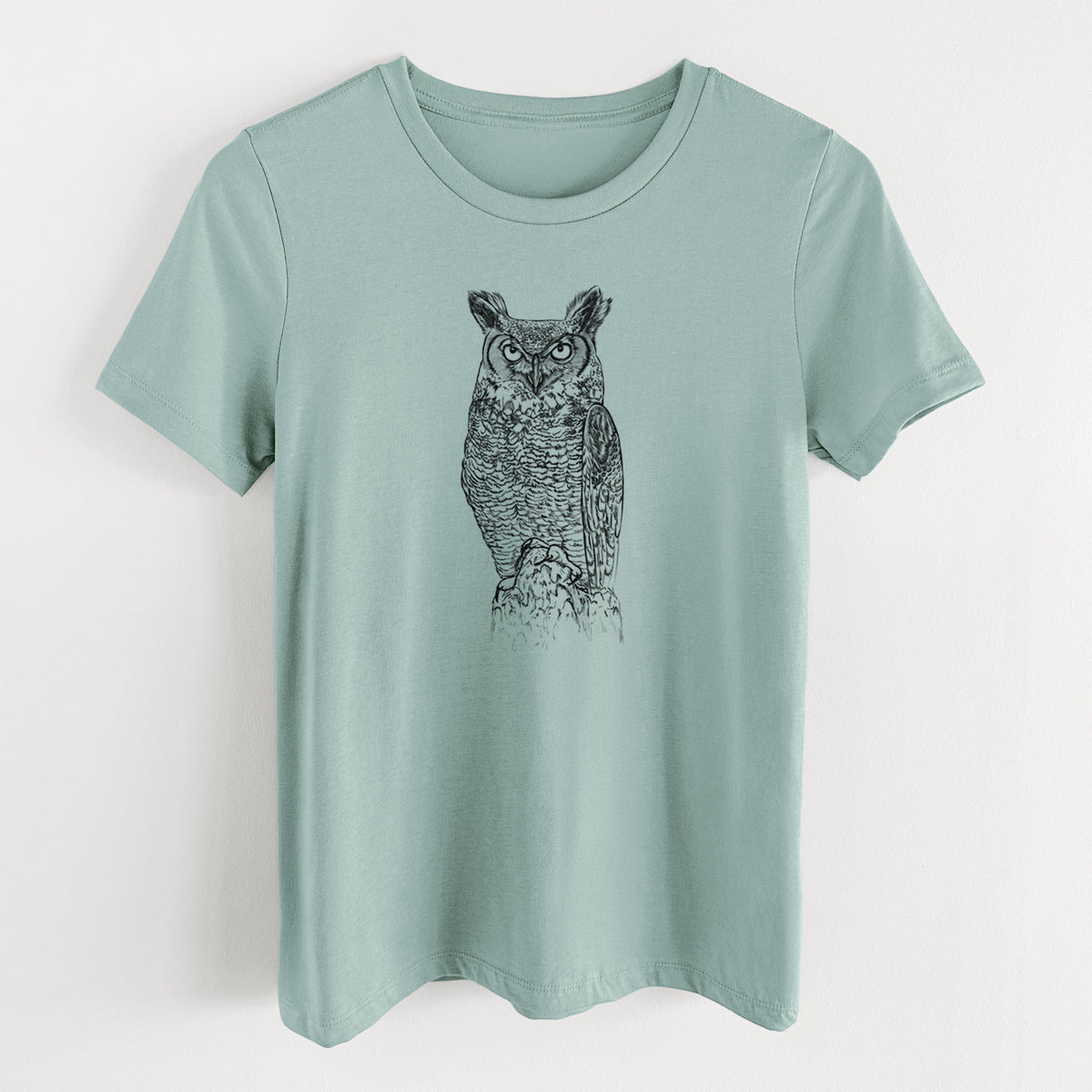 Dusty blue women's relaxed fit cotton t-shirt laid flat, printed with a detailed black ink illustration of a great horned owl standing upright with its ear tufts raised.