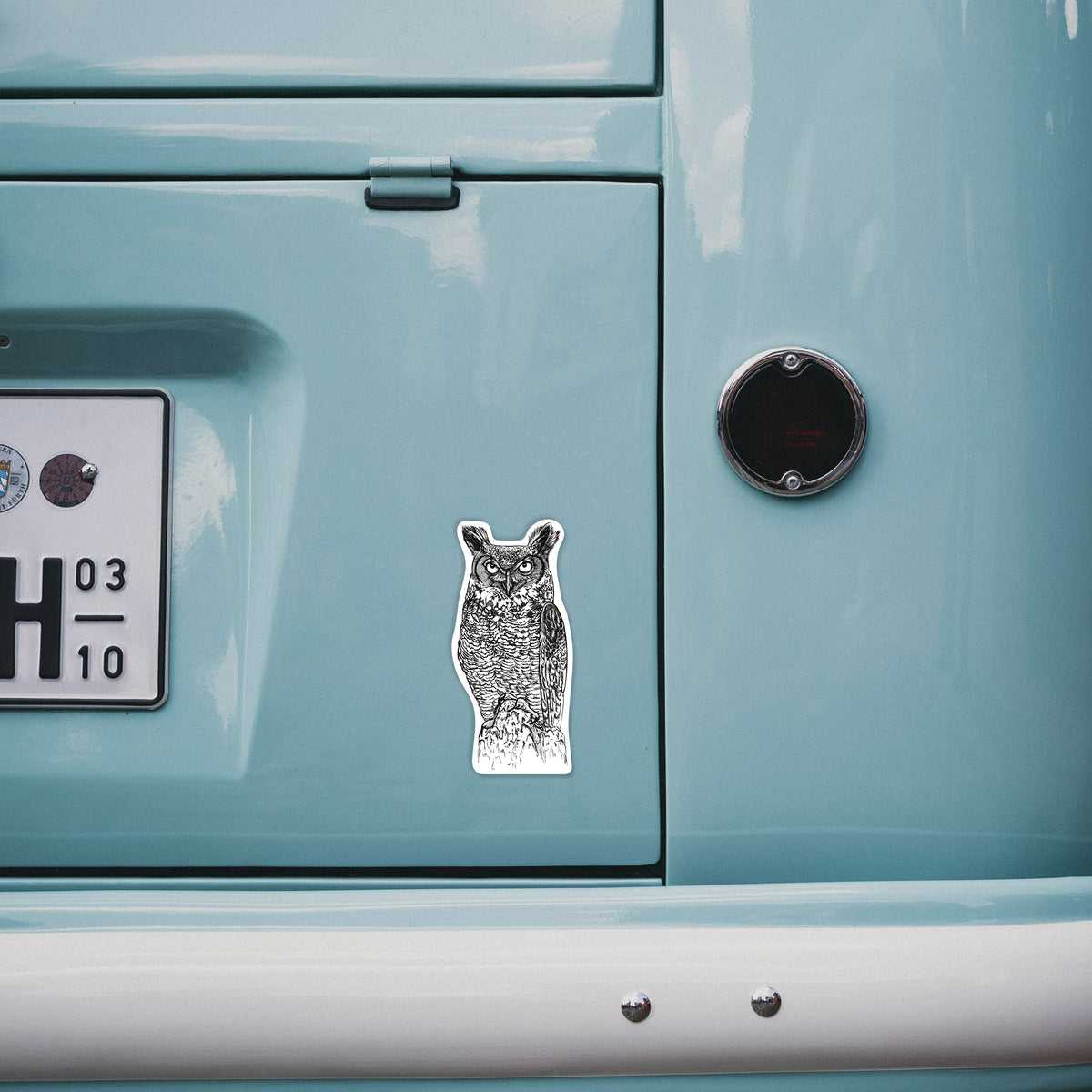 4 inch vinyl decal of a detailed black ink illustration of a great horned owl standing upright with its ear tufts raised on the back of a van.