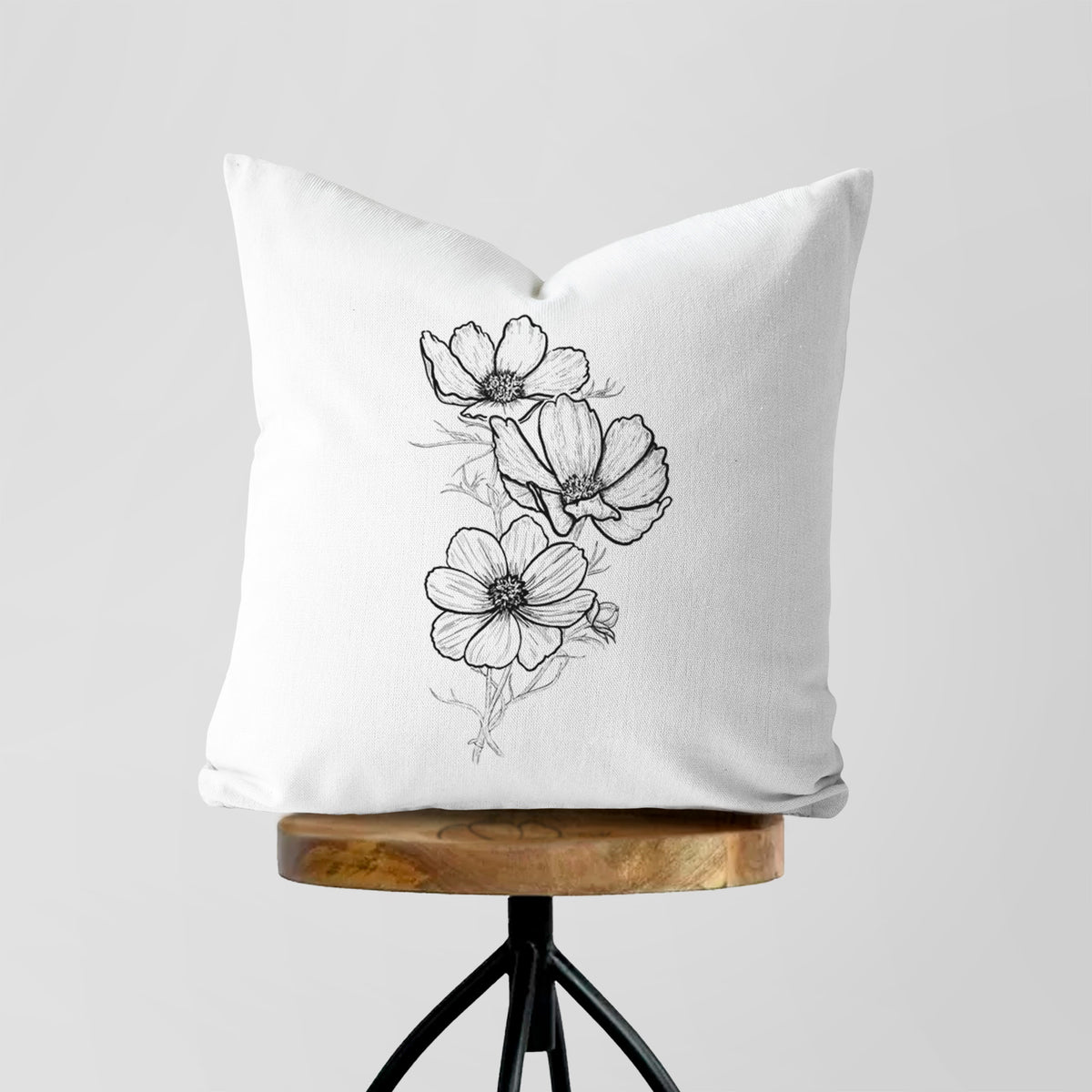 White pillow cover printed with a black ink line drawing of garden cosmos flowers on stems, on a wooden stool.