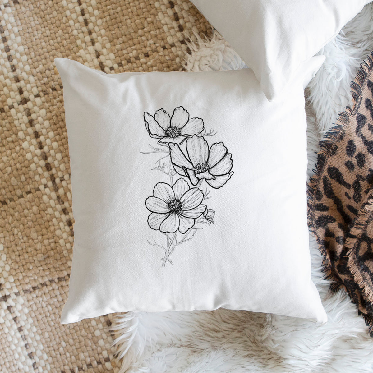 White pillow cover printed with a black ink line drawing of garden cosmos flowers on stems, on a woven chair.