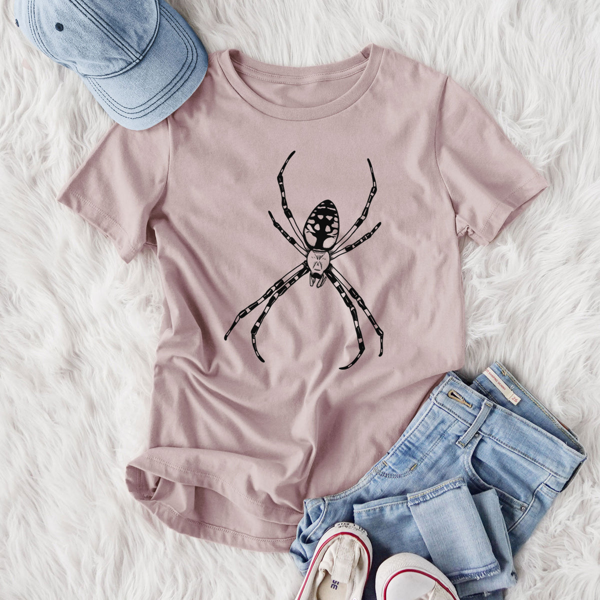 Women's relaxed fit cotton t-shirt printed with a detailed black ink illustration of a garden spider with long striped legs, styled flat on a white faux fur rug with jeans.