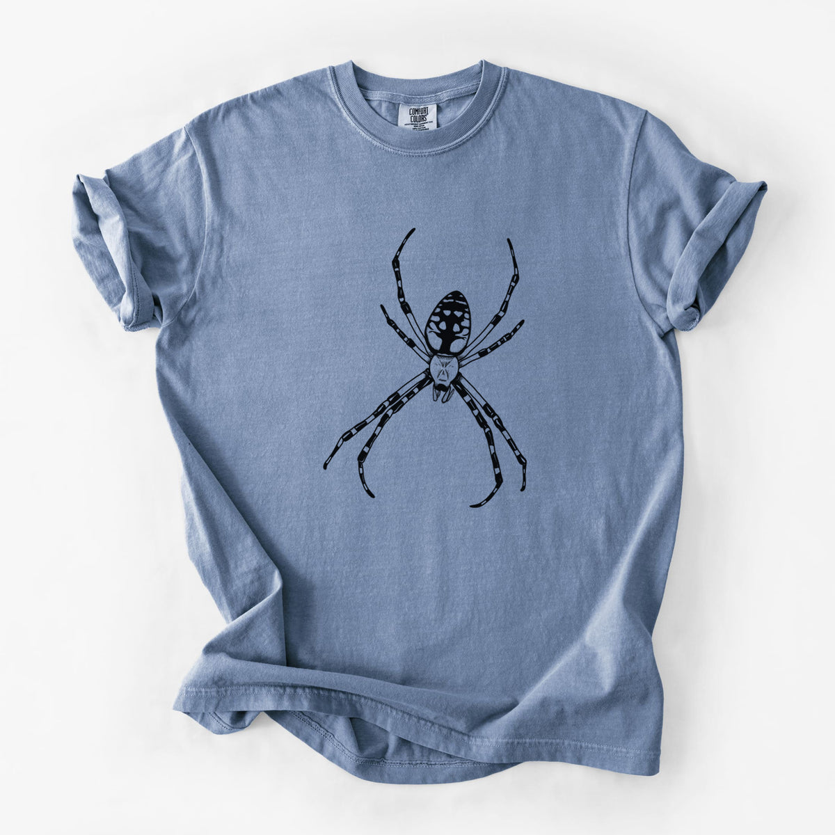 Blue jean Comfort Colors t-shirt laid flat, printed with a detailed black ink illustration of a garden spider with long striped legs.