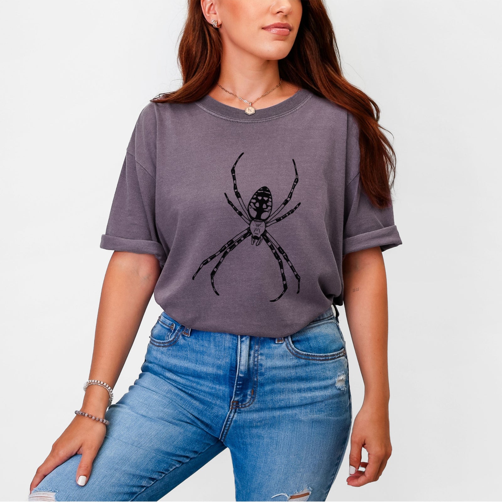 Blue jean Comfort Colors t-shirt laid flat, printed with a detailed black ink illustration of a garden spider with long striped legs.