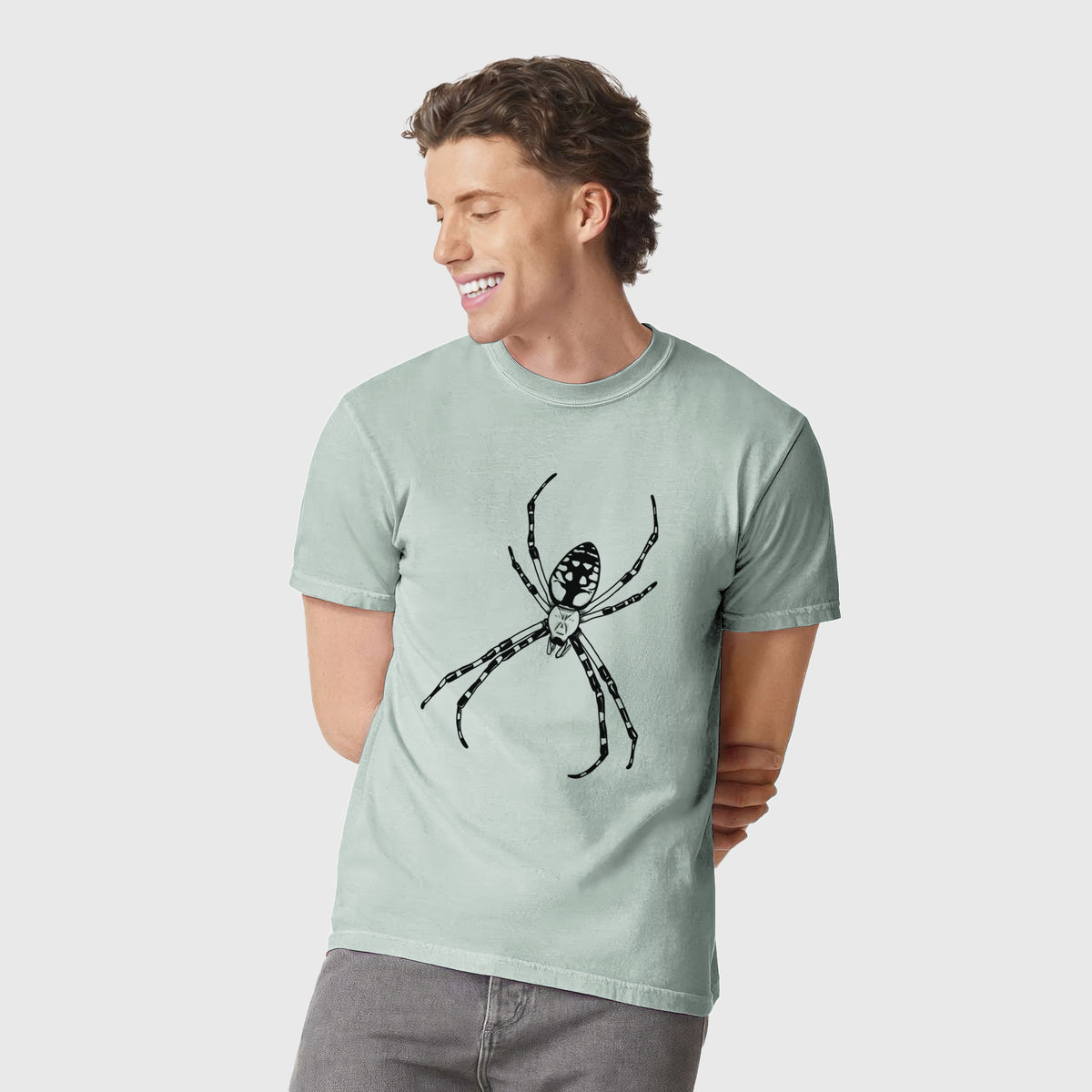 Man wearing a Comfort Colors t-shirt printed with a detailed black ink illustration of a garden spider with long striped legs.