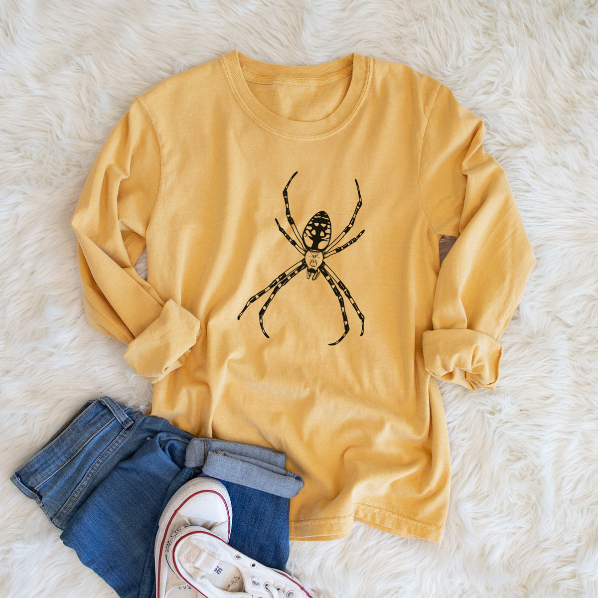 Golden wheat yellow Comfort Colors long sleeve shirt printed with a detailed black ink illustration of a garden spider with long striped legs, shown in a lifestyle photo.