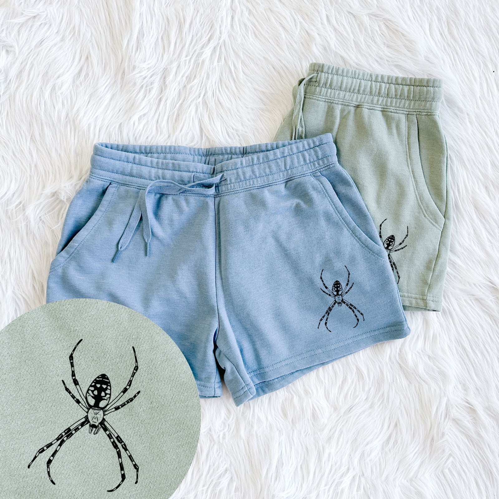 Two pairs of Cali Wave shorts in different colors printed with a detailed black ink illustration of a garden spider with long striped legs, with a close-up of the print.