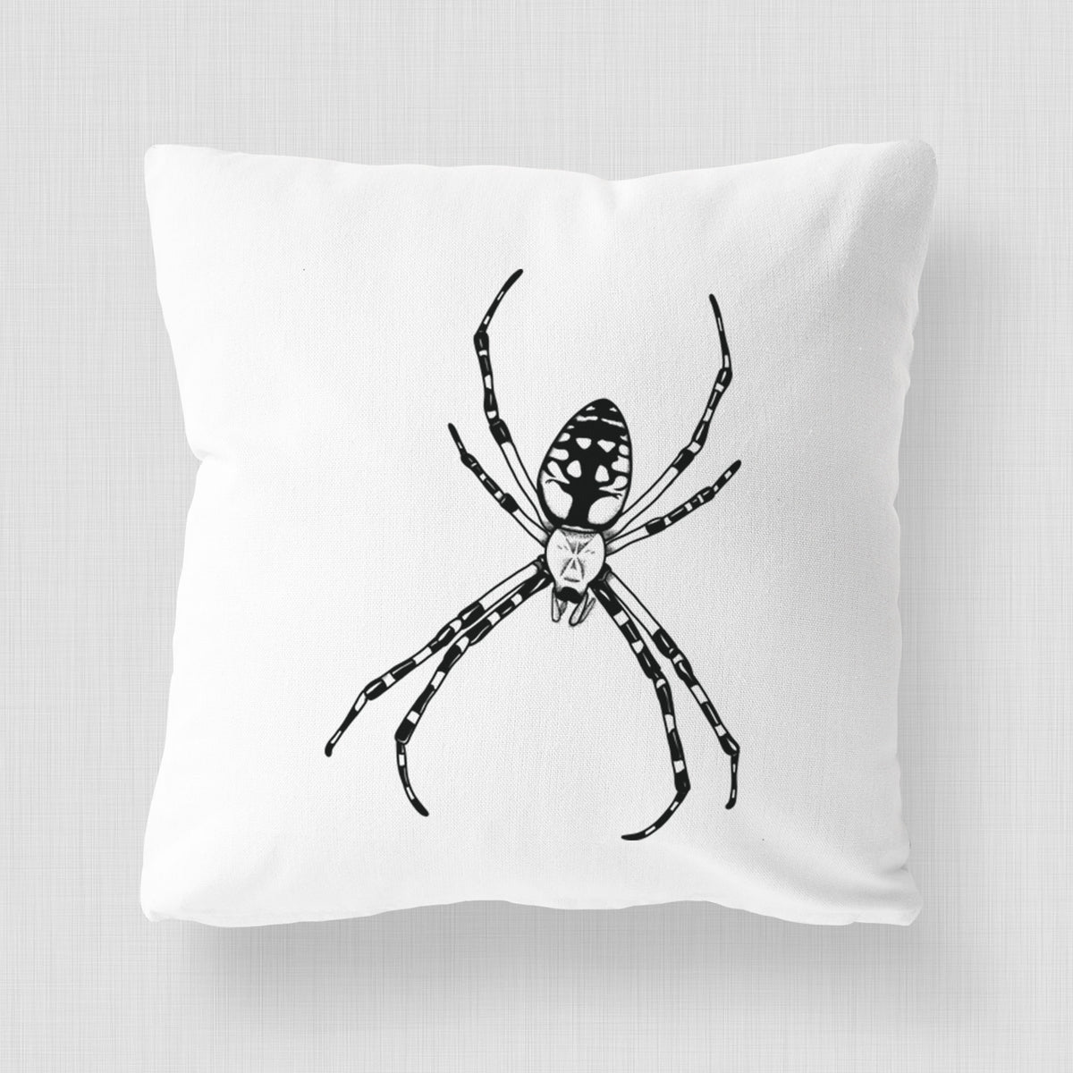 White pillow cover printed with a detailed black ink illustration of a garden spider with long striped legs.