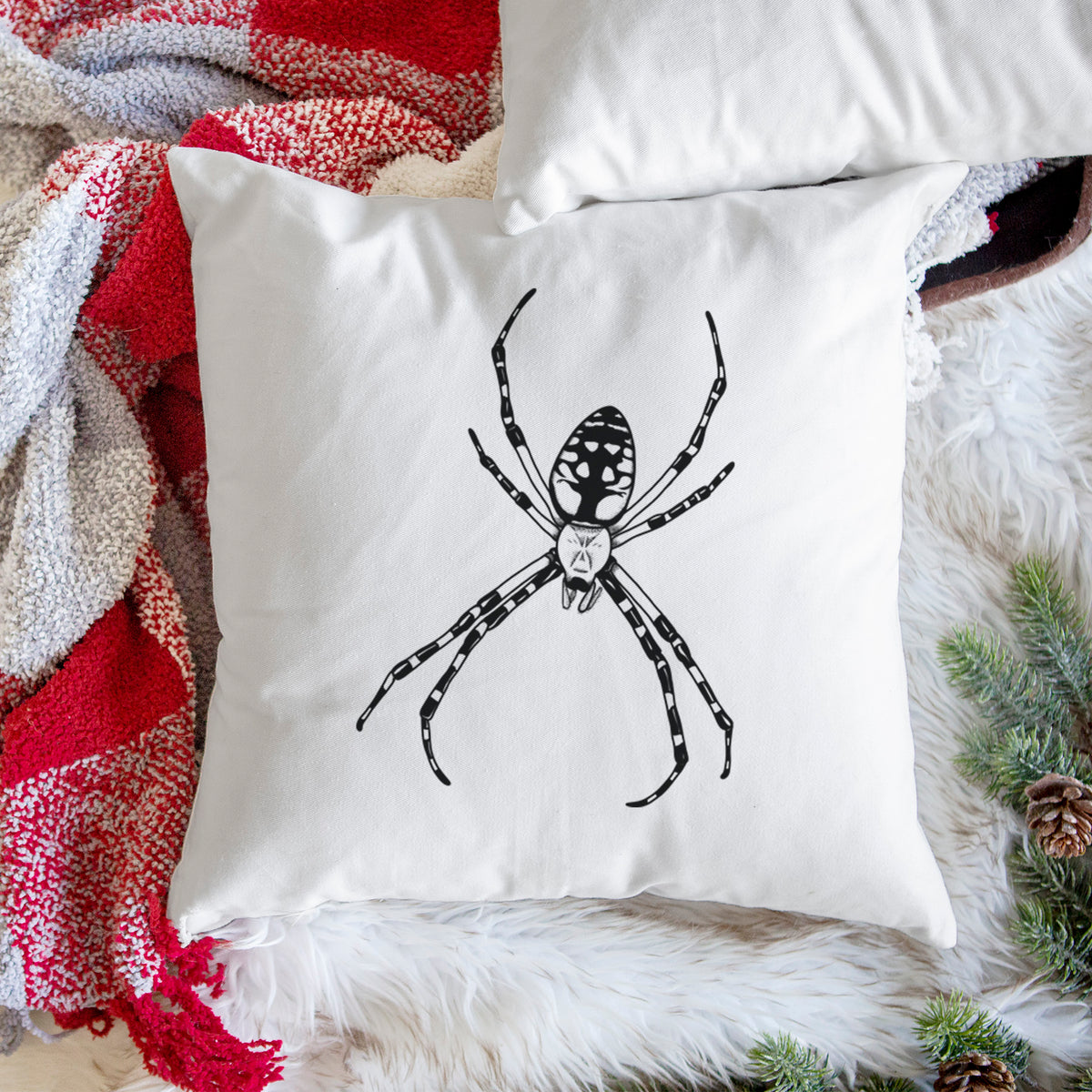 White pillow cover printed with a detailed black ink illustration of a garden spider with long striped legs, on a woven chair.